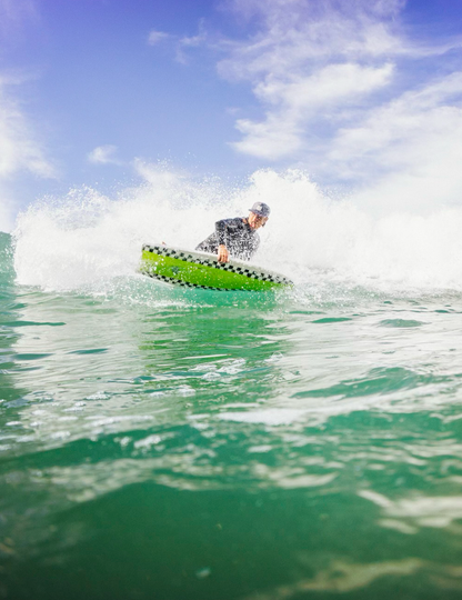 Person riding a green surfboard on a wave with a blue sky background